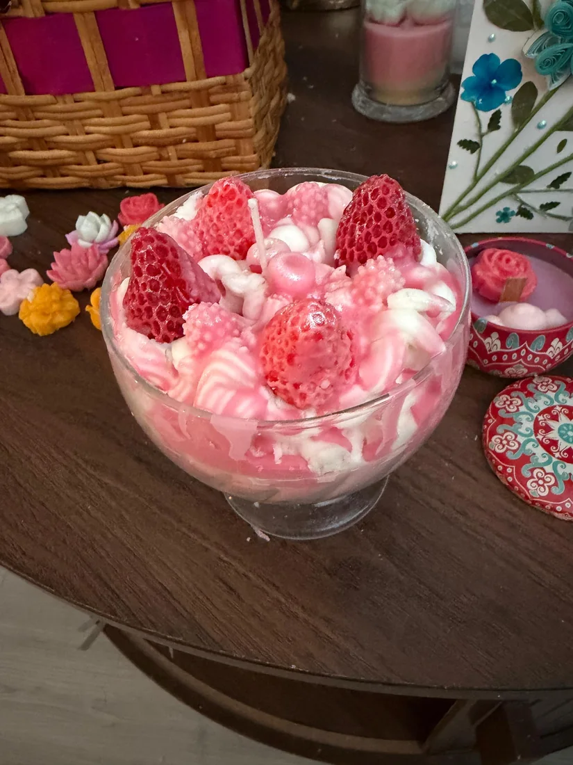 Vela rosada tipo postre servida en copa con figuras de fresas